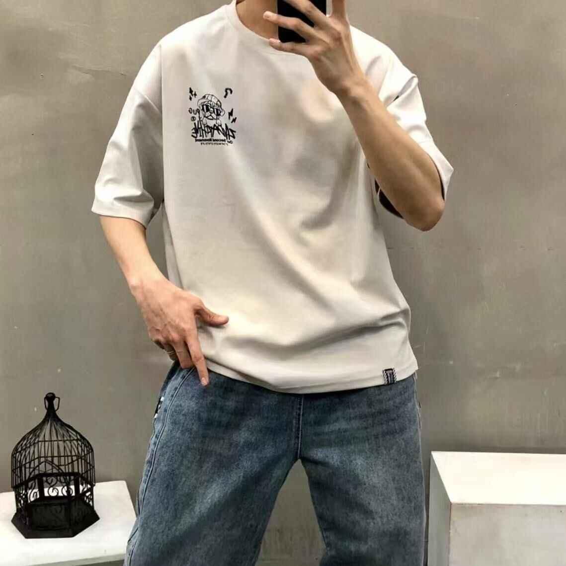 Beige oversized t-shirt with small black pug cartoon graphic, paired with blue jeans, casual style