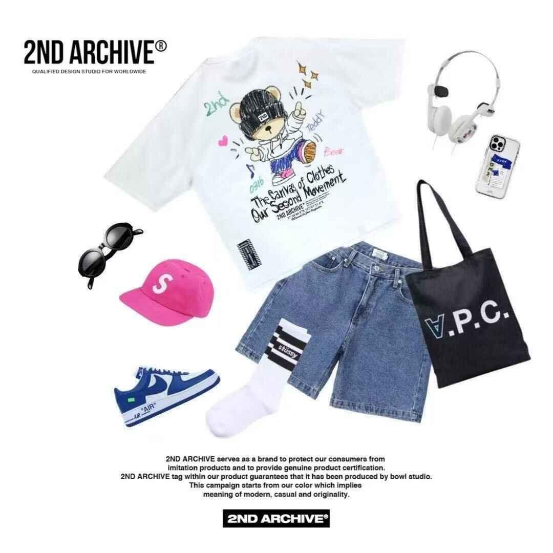 Streetwear flat lay with teddy bear graphic tee, denim shorts, blue sneakers, pink cap, black tote bag, sunglasses, and headphones.