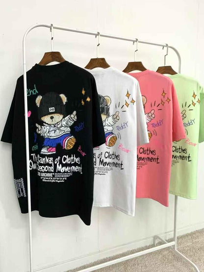 Colorful graphic t-shirts with teddy bear and text design hanging on a clothing rack.