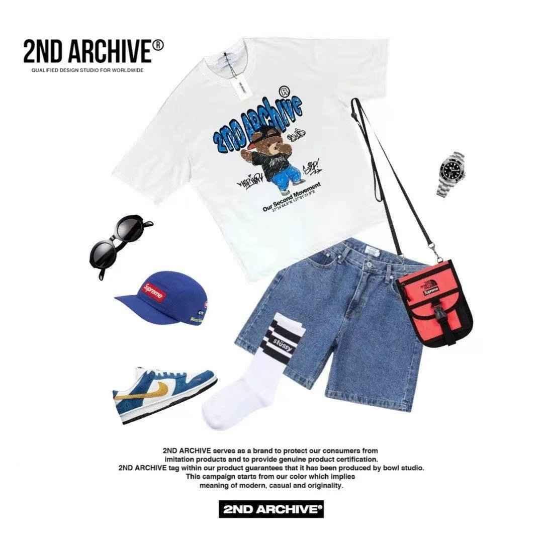 Casual streetwear outfit with bear graphic t-shirt, denim shorts, blue sneakers, cap, sunglasses, red crossbody bag, watch, and white socks, flat lay style.