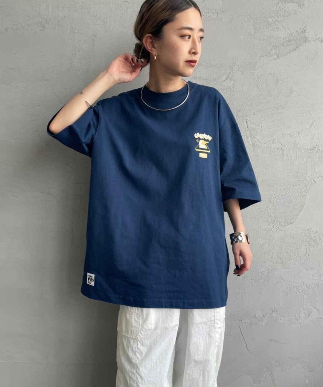Woman wearing oversized navy blue graphic tee with small yellow bird print, white pants, casual fashion style