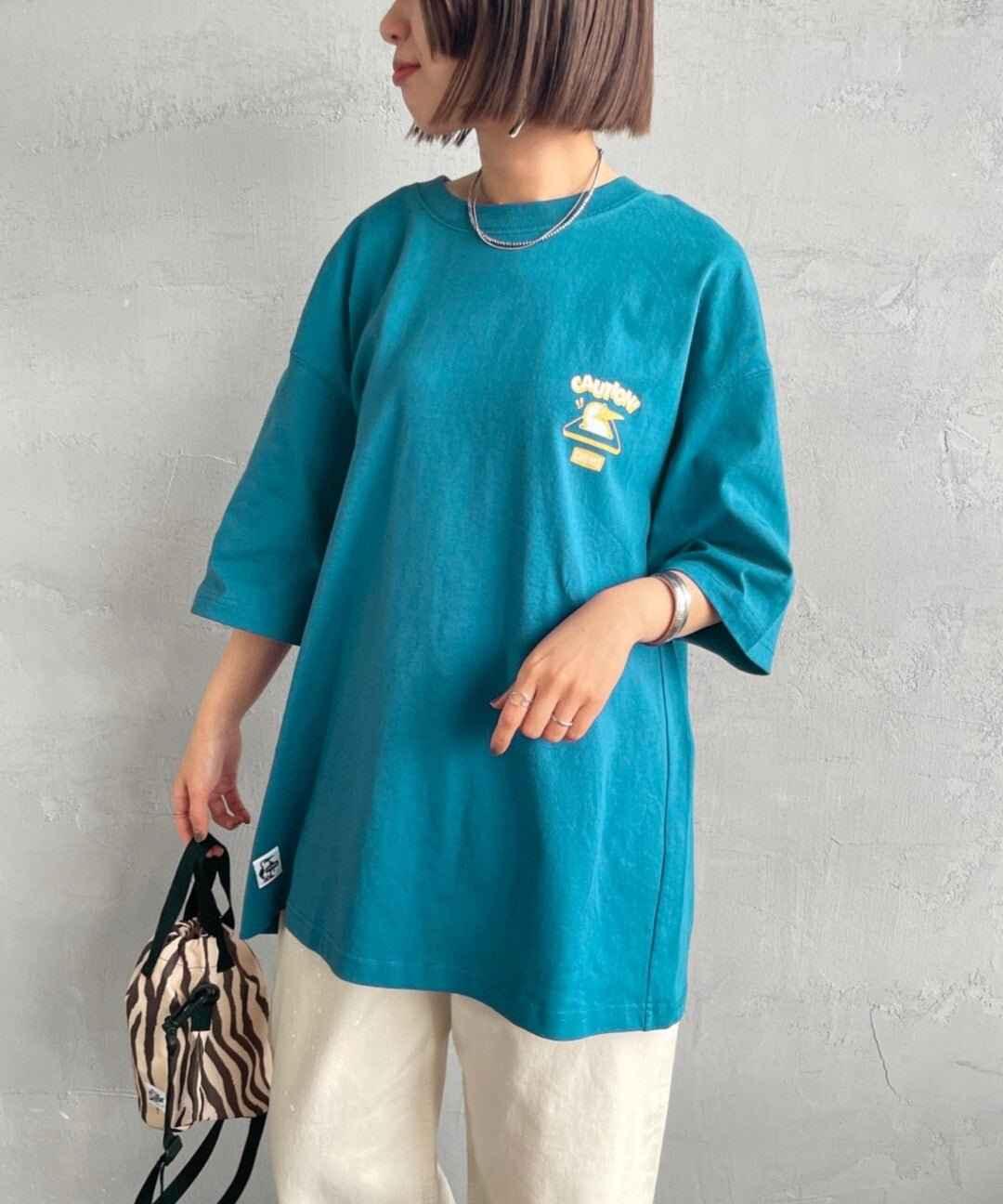 Woman wearing oversized teal booby bird graphic tee and white pants with zebra bag
