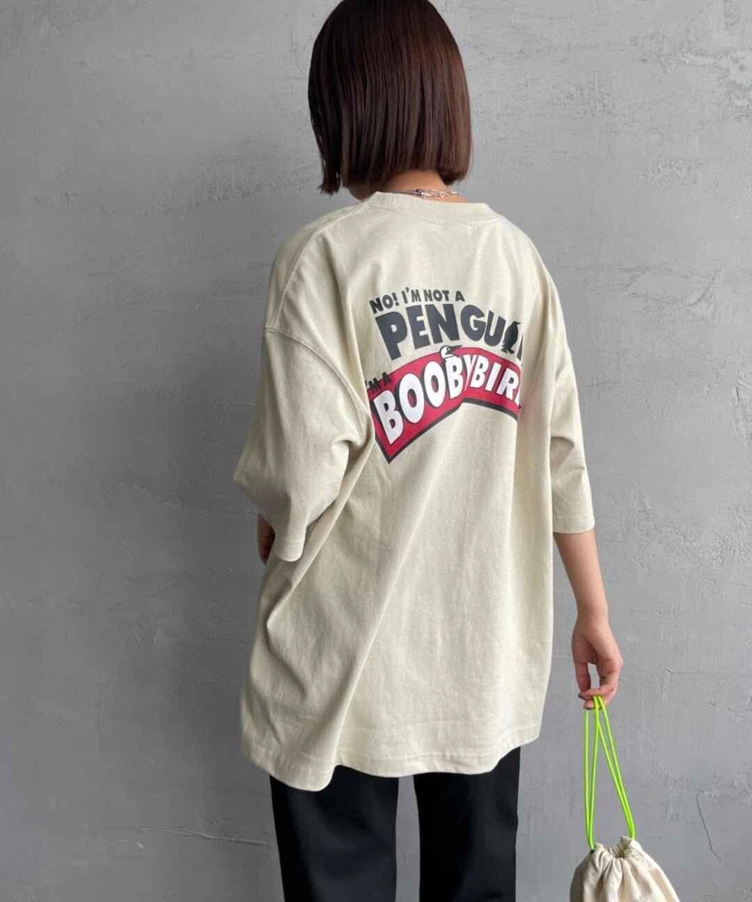 Back view of person wearing oversized beige Booby Bird graphic tee with bold text print